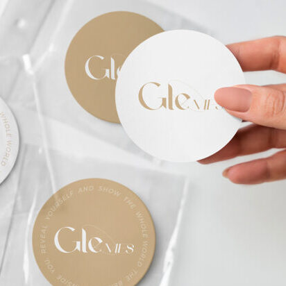 A collage of images showing hands applying branded circular stickers from various brands like Gleam Cafe, Aude Amorena, and Voor on different packaging materials including coffee cups, bubble mailers, and clear plastic bags.