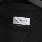 White clothing label with the text My Brand stitched onto a black fabric garment.