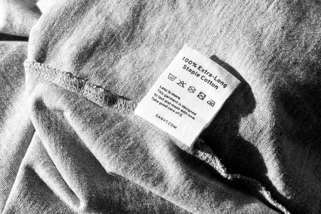 Clothing label on a gray fabric reading 100 percent extra-long staple cotton with care instructions.