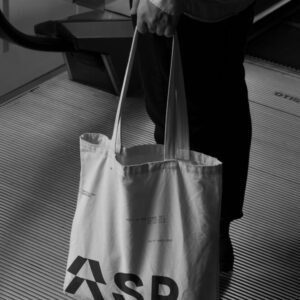 A person holding a white tote bag with bold "ASR" lettering and smaller text reading "Skill Up and Stand Out," in a monochrome setting.