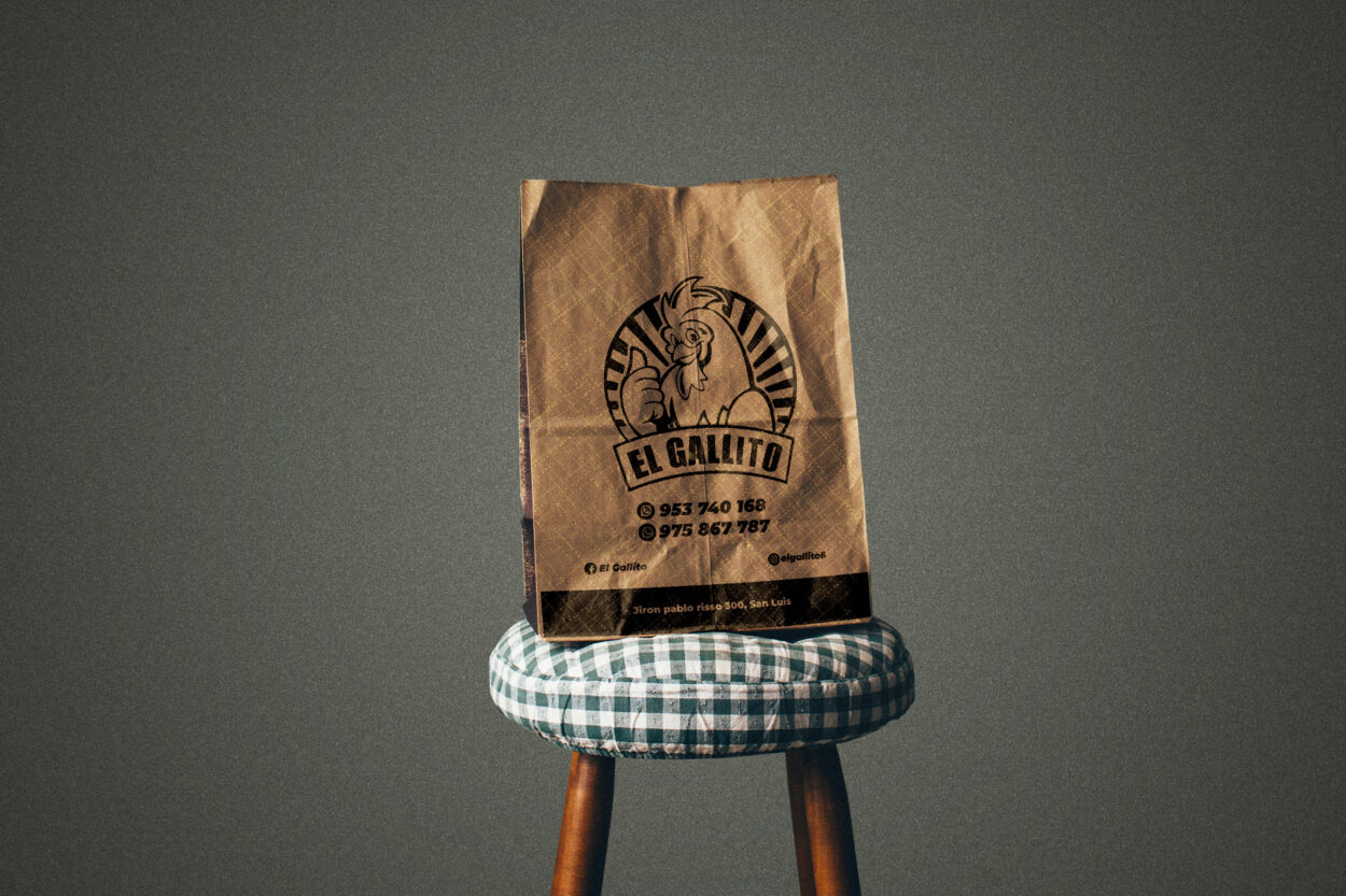 A brown paper bag with the logo and contact details of El Gallito printed in black ink displayed on a wooden stool with a checkered cushion.