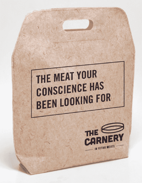 A biodegradable paper bag with a handle, featuring the text 'The Meat Your Conscience Has Been Looking For' and branding for 'The Carney In Vitro Meats.'