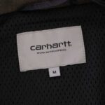 Carhartt Work in Progress label on a black mesh fabric with a white size tag labeled "M" below it.