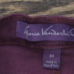 Purple clothing label with "Gloria Vanderbilt" written in cursive script, accompanied by a smaller size tag marked "8S" and the text "Made in Pakistan."